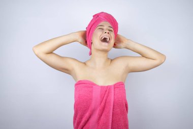 Genç, güzel bir kadın duş havlusu giyiyor. İzole edilmiş beyaz arka planda duruyor. Rahatlıyor ve esniyor.