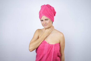 Genç, güzel bir kadın duş havlusu giyiyor. İzole edilmiş beyaz arka planda duruyor. Acı veren boynuna dokunuyor.