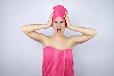Genç, güzel bir kadın duş havlusu takıyor. İzole edilmiş beyaz arka planda duruyor. Çılgınca ve korkmuş.