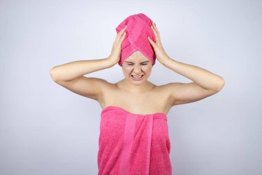 Genç, güzel bir kadın duş havlusu takıyor. İzole edilmiş beyaz arka planda duruyor. Baş ağrısı çekiyor, çaresiz ve stresli.