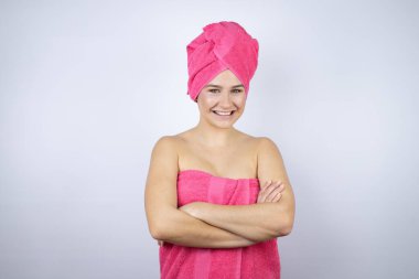 Genç, güzel bir kadın duş havlusu giyiyor. İzole edilmiş beyaz arka planda duruyor. Mutlu bir yüzü var.