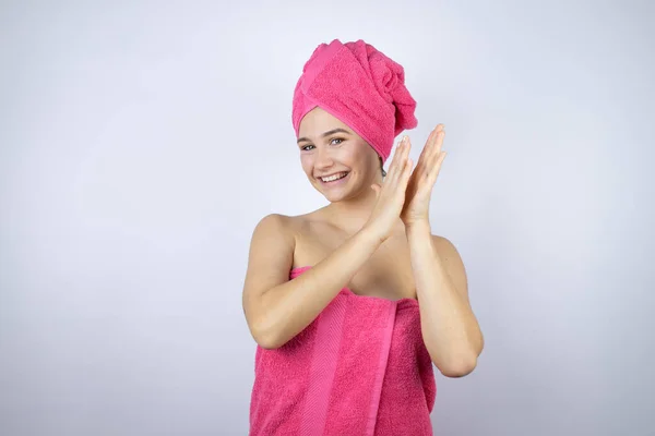 Genç, güzel bir kadın banyo üstüne duş havlusu giyiyor, izole edilmiş beyaz arka planda duruyor, alkışlıyor ve mutlu, neşeli, gururlu elleri alkışlıyor.