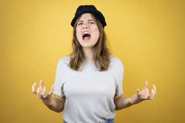 Fransız görünümlü güzel beyaz kız izole edilmiş sarı arka planda deli gibi bağırıyor ve agresif bir ifade ve kolla bağırıyor. Hayal kırıklığı konsepti.