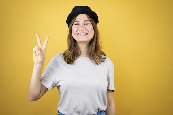 身穿法式衣服 头戴贝雷帽的年轻漂亮的高加索女孩 带着淡淡的黄色背景 带着自信和快乐的微笑 指点着二号手指 — 图库照片