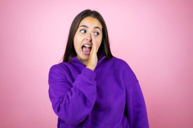 Genç, güzel bir kadın, kapalı pembe arka planda eşofman üstü giyip dudaklarına dokunuyor. Gizli dedikodular yayıyor, kötü niyetli konuşmalar fısıldıyor.