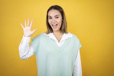 Sarı arka planda duran genç ve güzel bir kadın beş numarayı gösterip işaret ederken kendinden emin ve mutlu gülümsüyor.