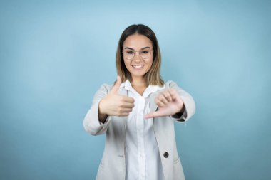 Tecrit edilmiş mavi arka planda genç bir iş kadını. Başparmak kaldırıyor, fikir ayrılığı yaşıyor ve anlaşamama ifadesi sergiliyor. Çılgın çatışma