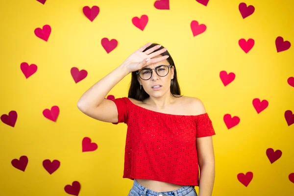 Young beautiful woman over yellow background with red hearts Touching forehead for illness and fever, flu and cold, virus sick