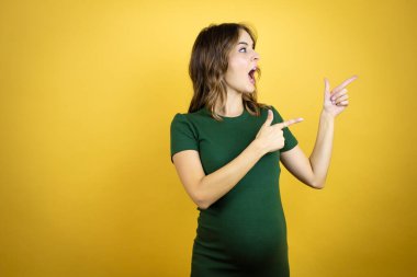 Güzel, esmer, hamile bir kadın, izole edilmiş sarı arka planda bebek bekliyor.