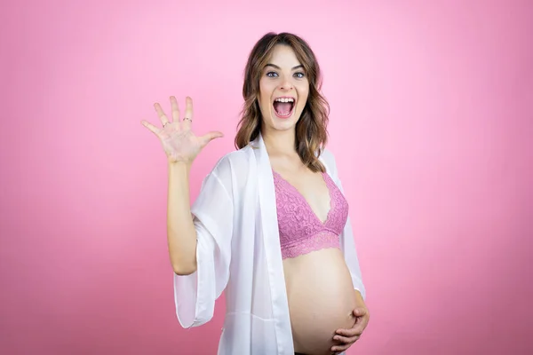 若いです美しいですブルネット女性妊娠予想赤ちゃん以上に隔離されたピンクの背景ショーとポイントアップとともに指番号5ながら笑顔自信と幸せ — ストック写真