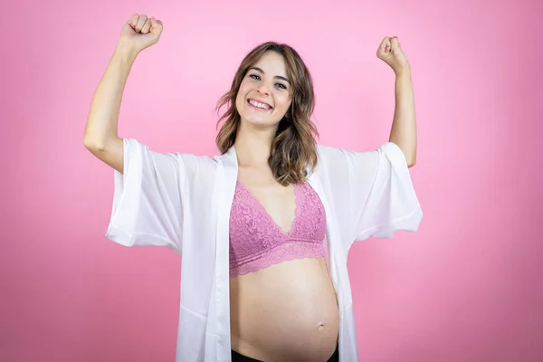 若いです美しいですブルネット女性予想赤ちゃん以上に孤立したピンクの背景非常に幸せと興奮メイキング勝者ジェスチャーとともに上げ腕 笑顔と悲鳴のために成功 — ストック写真