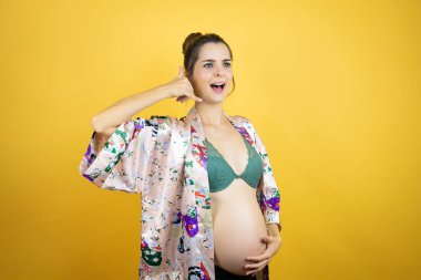 Genç, güzel bir kadın hamile. Sarı arka planda pijama giyiyor. Telefon hareketlerini telefonla konuşuyor gibi yapıyor.