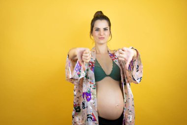 Güzel, hamile bir kadın, izole edilmiş sarı arka planda pijama giyiyor. Kızgın bir yüzü var.