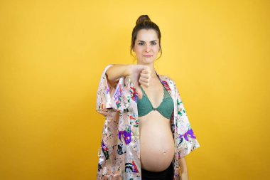 Güzel, hamile bir kadın, izole edilmiş sarı arka planda pijama giyiyor. Kızgın bir yüzü var.