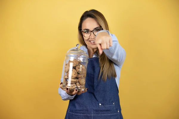 Young Hispanic Woman Wearing Baker Uniform Holding Cookies Jar Pointing — Stock Photo, Image