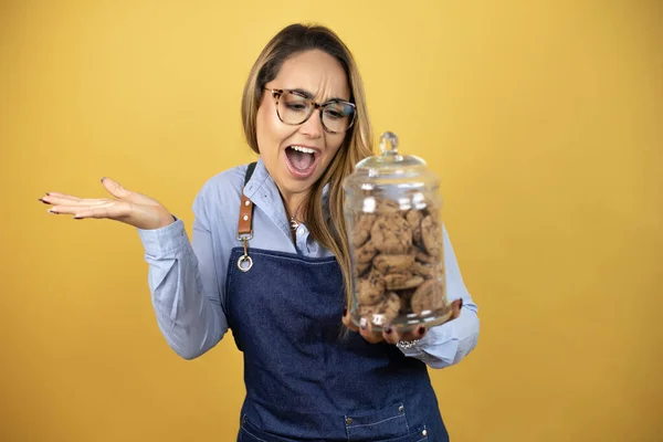 Young Hispanic Woman Wearing Baker Uniform Looking Cookies Jar Confused — Stock Photo, Image