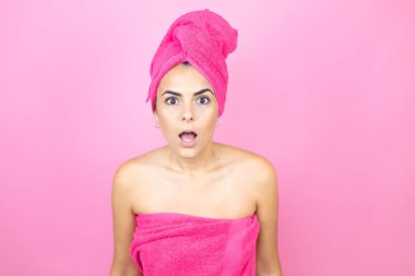 Genç, güzel bir kadın duş havlusu takıyor pembe arka planda dikiliyor korku ve şaşkınlık dolu bir ifade, korku ve heyecan dolu bir yüz..
