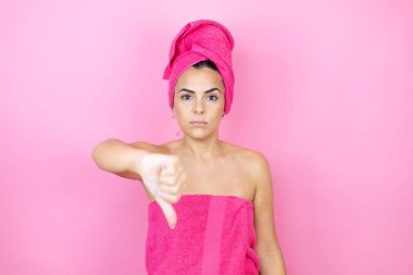Banyodan sonra duş havlusu takan genç ve güzel bir kadın. İzole edilmiş pembe arka planda duruyor. Kızgın bir yüzü var.