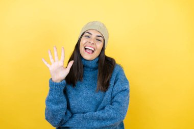 Mavi süveter ve yün şapka giyen genç ve güzel bir kadın beş numaralı parmaklarıyla onu gösterirken kendinden emin ve mutlu bir şekilde gülümsüyor.