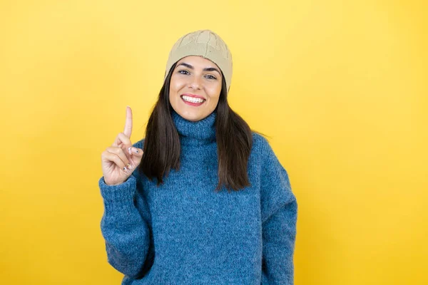年轻美丽的女人 身穿蓝色休闲装 头戴羊毛帽 带着自信和快乐的笑容 用手指着第一指尖 — 图库照片