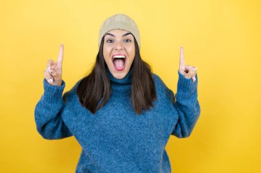 Mavi süveter ve yün şapka giyen genç ve güzel bir kadın kameraya bakıp parmaklarını kaldırıp kollarını kaldırdığında şaşırmış ve şaşırmıştı.