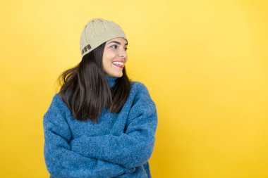 Mavi bir süveter ve yün şapka giyen genç ve güzel bir kadın. Taraf arayan, rahat profil pozu veren doğal bir yüz ve kendine güvenen bir gülümseme..