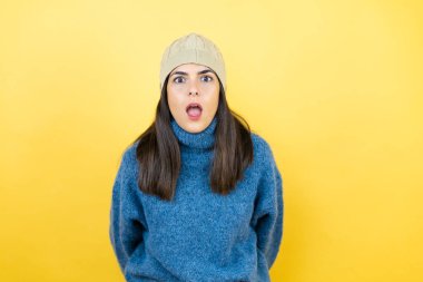 Mavi süveter ve yün şapka giyen genç ve güzel bir kadın şaşkınlık ve şaşkınlık dolu bir ifade, korku ve heyecan dolu bir yüz..