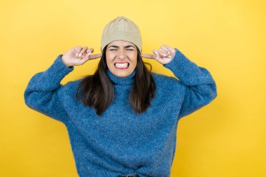 Gürültülü müzik sesi için mavi süveter ve kulakları parmaklarıyla kapatan yün şapka giyen genç ve güzel bir kadın. Sağır kavramı.