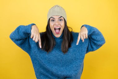 Mavi süveter ve yün şapka giyen genç ve güzel bir kadın şaşırdı, aşağı baktı ve parmaklarıyla işaret etti ve kollarını kaldırdı.