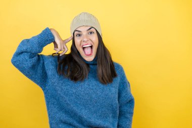 Mavi süveter giyen, yün şapkalı, gülümseyen ve kafasında parmaklarıyla bir fikri olduğunu düşünen genç ve güzel bir kadın..