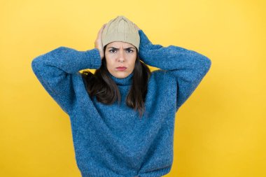 Mavi süveter ve yün şapka giyen genç ve güzel bir kadın yorgun ve elleri başının üzerinde sıkılmış görünüyor.