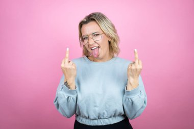 Young caucasian woman wearing sweatshirt over pink background showing middle finger doing fuck you bad expression, provocation and rude attitude. screaming excited