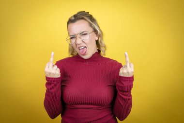 Young caucasian woman wearing casual red t-shirt over yellow background showing middle finger doing fuck you bad expression, provocation and rude attitude. screaming excited