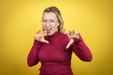 Young caucasian woman wearing casual red t-shirt over yellow background smiling funny doing claw gesture as cat, aggressive and sexy expression