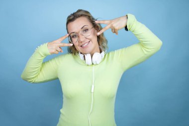 Mavi arka planda kulaklık takan genç, beyaz bir kadın barış sembolü yapıyor. Yüzünde parmaklar, gülümseyerek zaferini gösteriyor.