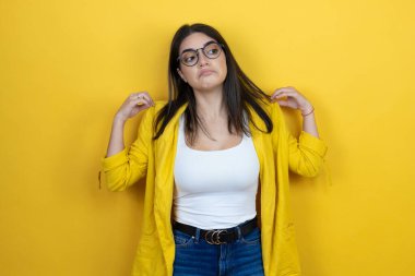 Sarı arka planda sarı ceket giyen esmer iş kadını tişörtünü başarıyla tutuyor.