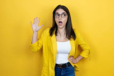 Sarı arka planda sarı ceket giyen genç esmer iş kadını beş numaralı parmaklarıyla işaret ederken kendinden emin ve mutlu gülümsüyor.