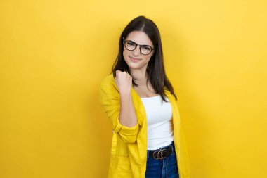 Sarı arka plan üzerine sarı ceket giyen genç esmer iş kadını öfkeyle bağırırken kızgın ve öfkeli bir şekilde yumruğunu kaldırıyor. Öfke ve agresif kavram.