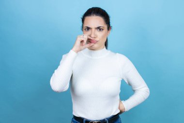 Beyaz süveter giyen beyaz bir kadın mavi arka plan ağzı ve dudakları parmaklarıyla fermuar gibi kapalı. Gizli ve sessiz, tabu konuşması