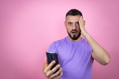 Pembe arka plan üzerine sıradan tişörtler giyen genç yakışıklı adam telefonda endişeli bir ifadeyle sohbet ediyor.