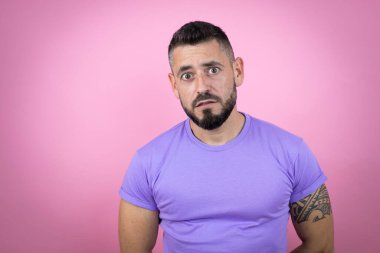 Pembe arka plan üzerine gündelik tişört giyen genç yakışıklı adam şaşkınlık ve şaşkınlık dolu bir ifade, korku ve heyecan dolu bir yüz ifadesiyle dehşete düşmüş ve şok olmuştu..