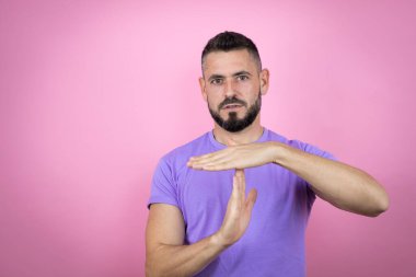 Pembe arka plan üzerine gündelik tişört giyen genç yakışıklı bir adam. Elleriyle jest yapıyor, sinirli ve ciddi bir yüz ifadesi takınıyor.