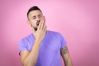 Pembe arka plan üzerine gündelik tişört giyen genç yakışıklı adam ağzıyla esnemekten sıkılmış. Huzursuz ve uykulu..