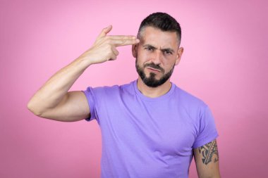 Pembe arka planda sıradan tişörtler giyen genç yakışıklı bir adam kendini vuruyor ve öldürüyor silah gibi el ve parmakları işaret ediyor, intihar jesti..