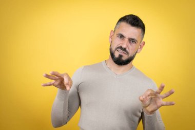 Sakallı yakışıklı bir adam sarı arka planda süveter giyiyor tiksindirici bir ifade takınıyor ve tiksindirici bir yüz ifadesi takınıyor. Can sıkıcı bir kavram.