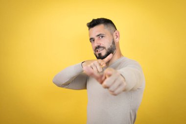 Sarı arka planda sakallı yakışıklı adam seni ve kamerayı işaret ediyor, gülümsüyor olumlu ve neşeli.