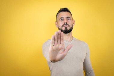 Sarı arka planda süveter giyen sakallı yakışıklı adam ciddi ve avucunun içi gibi şarkı söylemeyi kesiyor..