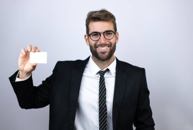 Takım elbiseli genç iş adamı gülümsüyor ve elinde beyaz kart tutuyor.