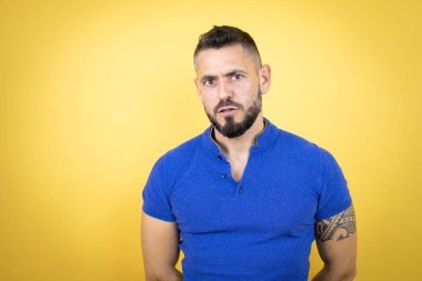 Sarı arka plan üzerinde mavi polo tişört giyen yakışıklı adam şaşırmış ve şaşırmış bir ifadeyle, korkuyla ve heyecanlı yüzüyle şok olmuştu..