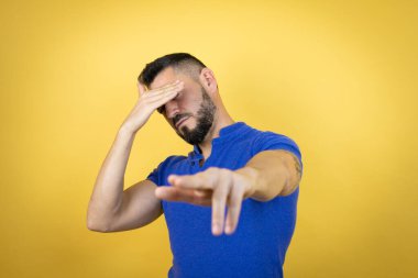 Sarı arka plan üzerine mavi polo tişörtü giyen yakışıklı adam elleriyle gözlerini kapatıyor ve üzgün ve korku ifadeleriyle jest yapıyor. Utanç verici ve olumsuz bir kavram..